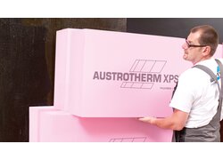 Arbeiter hält rosa Wärmedämmplatten mit Markenaufdruck an Wand.