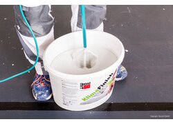 KlimaFinish Spachtel 20kg, Material aufrühren, Eimer zwischen den Füßen eines Mannes auf dem Boden stehend