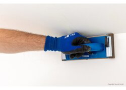 KlimaFinish Spachtel 20kg, Schleifen der Ecken bis zur Glätte, Arm eines Mannes mit blauen Handschuhen