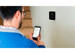 Mann, der die Smartphone-App Genius benutzt, um ein an der Wand montiertes Smart-Home-Gerät zu steuern.