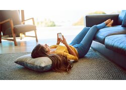 Frau, liegend auf Wohnzimmerboden, mit Handy in Hand, betrachtet die Genius UserApp