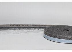 graue Rolle eines Schaumstoffstreifens mit blauer Klebefläche, auf dem Text zu einer Fußbodenheizungszone ("Hier liegt die NORIT Fußbodenheizzone") aufgedruckt ist.