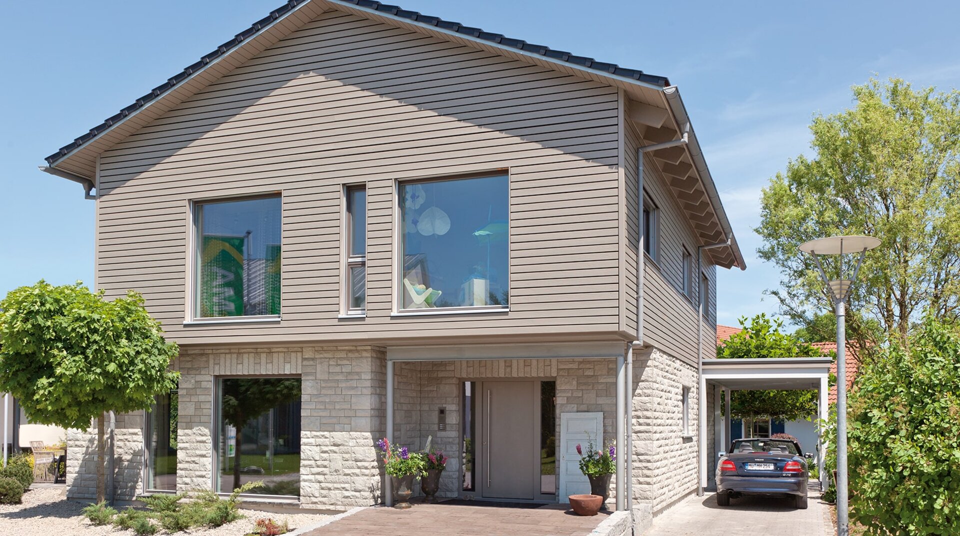 Frontansicht des Hauses mit Carport und großem Eingangsbereich. Große Fenster lassen viel Licht in das Gebäude